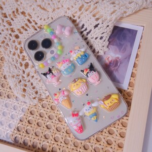 May include: A clear phone case with a white background and colorful cartoon characters. The characters are holding ice cream cones, cupcakes, and other treats. There are also colorful beads and glitter on the case.