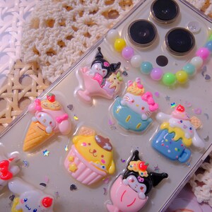 May include: A clear phone case with a variety of colorful cartoon characters and a beaded charm. The characters include a cat, a dog, a rabbit, and a bear. The case is decorated with glitter and stars.