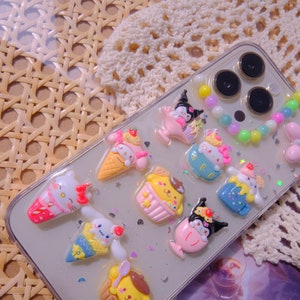 May include: A clear phone case with colorful cartoon characters and a beaded charm. The characters are themed around ice cream and desserts. The case is decorated with glitter.
