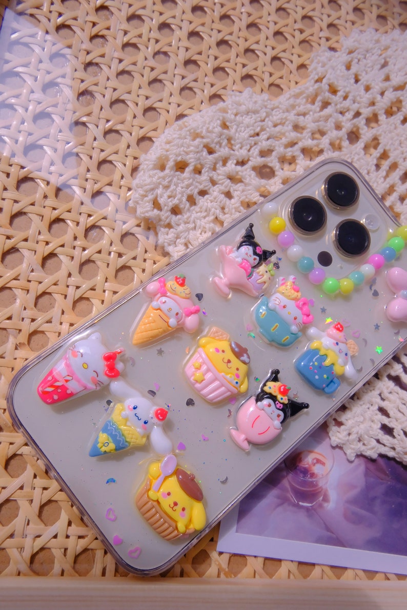 May include: A clear phone case with colorful cartoon characters and a beaded charm. The characters are themed around ice cream and desserts. The case is decorated with glitter.