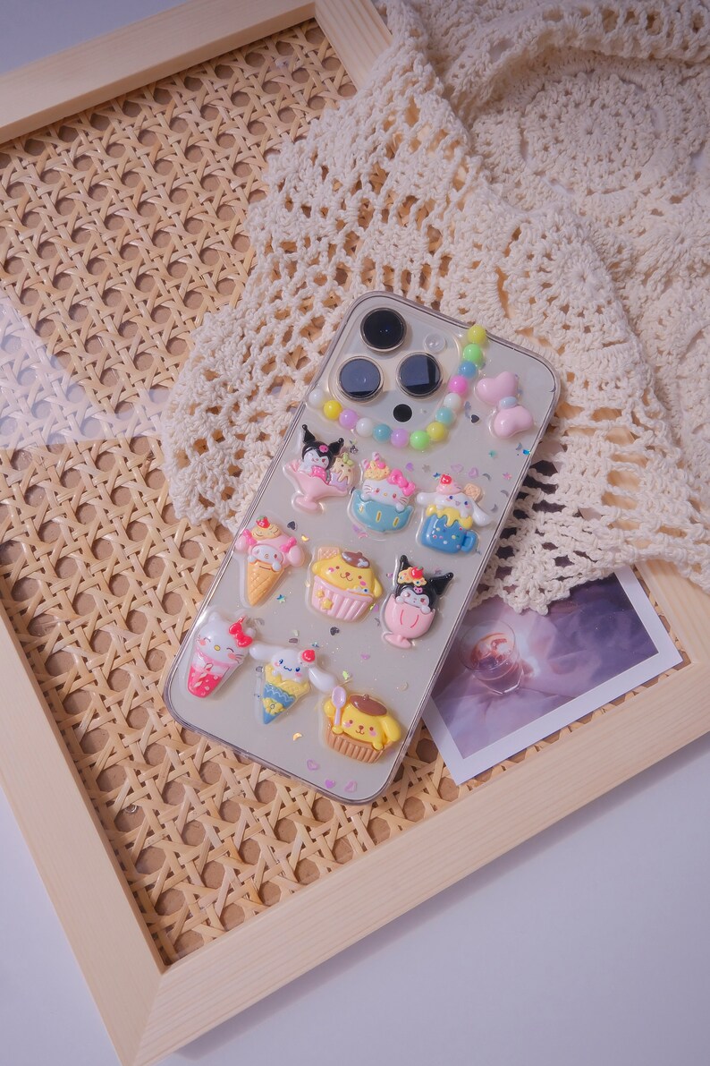 May include: A clear phone case with a colorful beaded charm and various cartoon character stickers. The case is decorated with glitter and hearts.