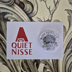 May include: A white card with red text and a button. The card reads "QUIET NISSE" with a red graphic. The button says "BORN TO DALLY FORCED TO DILLY" with a hedgehog illustration. The background has a floral design.