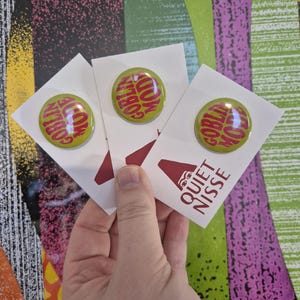 May include: Three round green buttons with the words "GOBLIN MODE" in red text. Each button is attached to a white card with a red graphic and the text "QUIET NISSE". The background features colorful abstract patterns.