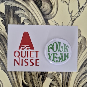 May include: A white card with the text "QUIET NISSE" in red and a red graphic. A round button with the words "folk YEAH" in green is next to the card. The background has a floral design.