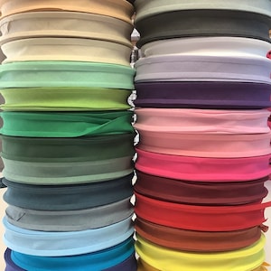 May include: A stack of 20 rolls of bias binding in various colours, including brown, beige, green, blue, red, and white. The binding is folded and ready to be used for sewing projects.