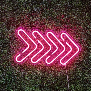 May include: A pink neon sign shaped like an arrow pointing to the right, mounted on a green wall.