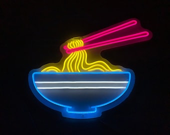 Puede incluir: Señal de neón que representa un tazón de fideos con palillos. El tazón es azul, los fideos son amarillos y los palillos son rosas.