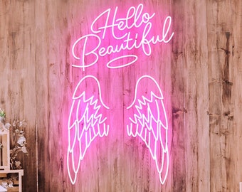 May include: Pink neon sign with the words "Hello Beautiful" and a pair of angel wings. The sign is hanging on a wooden wall with floral decorations.