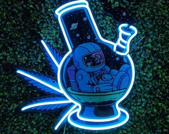 Puede incluir: Un letrero de neón azul que representa una pipa de agua con un astronauta en su interior. La pipa de agua está rodeada por una hoja de marihuana estilizada. El astronaute lleva un traje espacial y está sentado en una pequeña nave espacial. El fondo del letrero es un cielo nocturno estrellado.