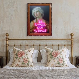 Puede incluir: Un dormitorio con una cama, cojines florales y una obra de arte enmarcada. La obra presenta un retrato cl&aacute;sico con el texto de ne&oacute;n "BE SAVAGE, NOT AVERAGE". L&aacute;mparas con pantallas plisadas est&aacute;n en las mesitas de noche.