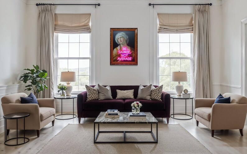 Puede incluir: Interior de sal&oacute;n con un sof&aacute; morado oscuro, dos sillones beige y una mesa de centro de m&aacute;rmol. Una obra de arte enmarcada con el texto "BE SAVAGE NOT AVERAGE" cuelga sobre el sof&aacute;. La habitaci&oacute;n tiene grandes ventanas y cortinas de tonos neutros.