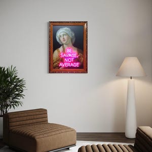 Puede incluir: Una obra de arte enmarcada con un retrato cl&aacute;sico y un letrero de ne&oacute;n rosa. El letrero dice "BE SAVAGE, NOT AVERAGE". La obra de arte est&aacute; en un marco marr&oacute;n adornado, en una pared blanca. La habitaci&oacute;n incluye una silla marr&oacute;n y una l&aacute;mpara de pie blanca.