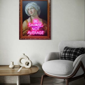 Puede incluir: Obra de arte enmarcada con un retrato cl&aacute;sico y texto rosa ne&oacute;n que dice "BE SAVAGE, NOT AVERAGE". El marco es marr&oacute;n y la obra cuelga de una pared blanca. La imagen es parte de un sal&oacute;n moderno con una silla y una mesa.