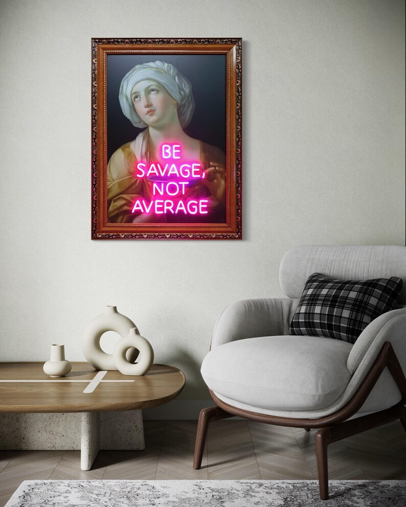 Puede incluir: Obra de arte enmarcada con un retrato cl&aacute;sico y texto rosa ne&oacute;n que dice "BE SAVAGE, NOT AVERAGE". El marco es marr&oacute;n y la obra cuelga de una pared blanca. La imagen es parte de un sal&oacute;n moderno con una silla y una mesa.
