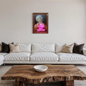 Puede incluir: Una obra de arte enmarcada con un retrato cl&aacute;sico y el texto de ne&oacute;n "BE SAVAGE NOT AVERAGE". La obra de arte cuelga sobre un sof&aacute; blanco con cojines. Una mesa de centro de madera con un cuenco blanco est&aacute; frente al sof&aacute;.