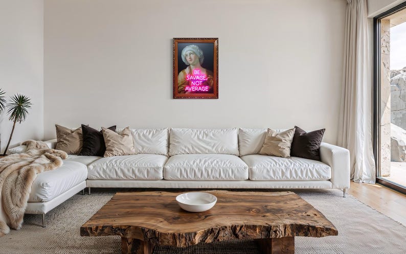 Puede incluir: Una obra de arte enmarcada con un retrato cl&aacute;sico y el texto de ne&oacute;n "BE SAVAGE NOT AVERAGE". La obra de arte cuelga sobre un sof&aacute; blanco con cojines. Una mesa de centro de madera con un cuenco blanco est&aacute; frente al sof&aacute;.