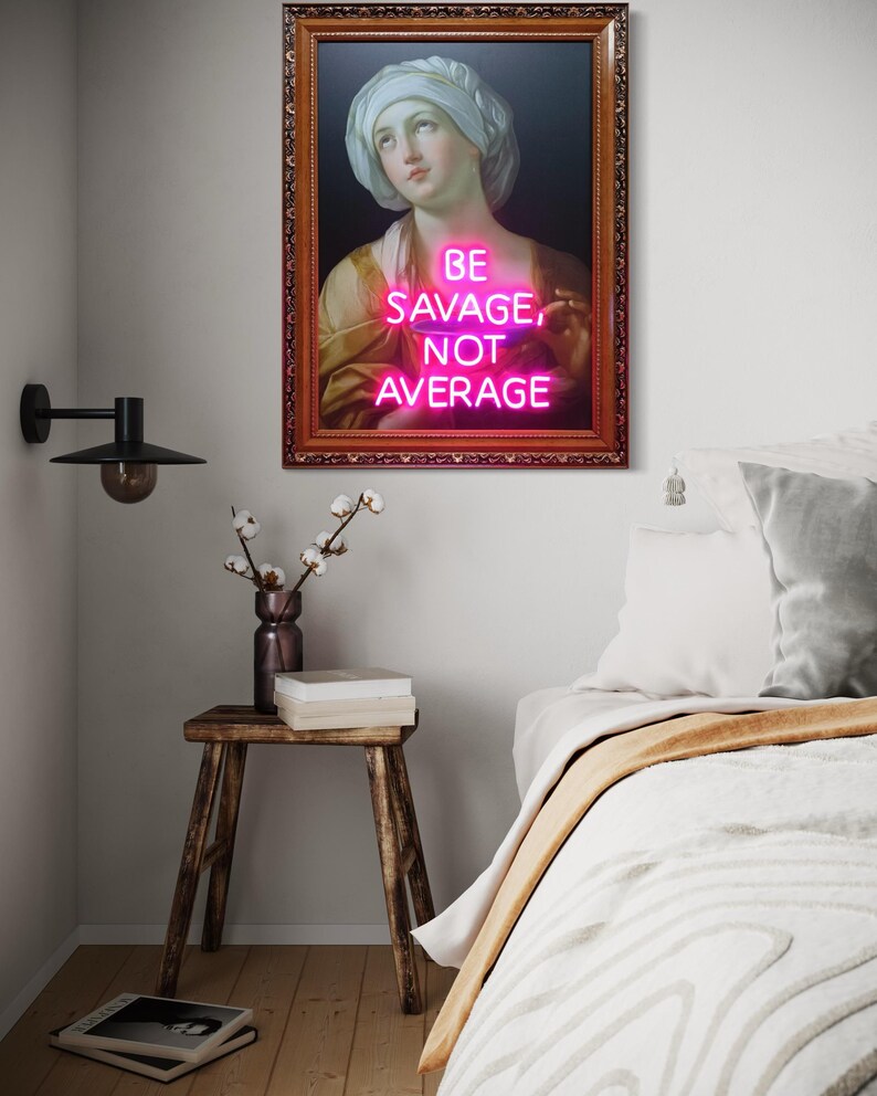 Puede incluir: Una obra de arte enmarcada con un retrato cl&aacute;sico y un letrero de ne&oacute;n. El letrero de ne&oacute;n rosa dice "BE SAVAGE, NOT AVERAGE". El marco adornado rodea la imagen. La obra de arte se exhibe sobre un taburete de madera y una cama.