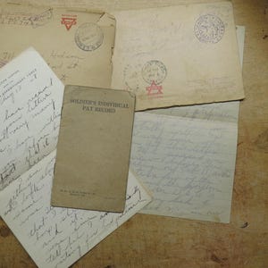May include: A collection of vintage beige paper documents including a Soldier's Individual Pay Record booklet, several handwritten letters with cursive ink, and weathered envelopes featuring circular postmarks and red triangular logos.