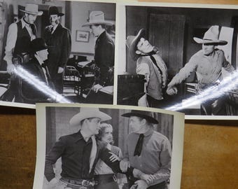 Op de afbeelding: Zwart-witfoto's van scènes uit een westernfilm. De afbeeldingen tonen acteurs in cowboyhoeden, pakken en kleding uit die tijd, die verschillende scènes met dramatische uitdrukkingen en poses uitbeelden. De foto's zijn gerangschikt op een houten oppervlak.