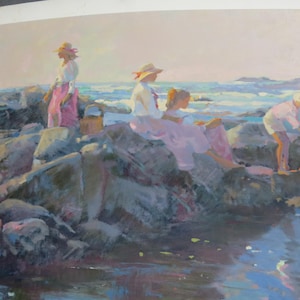 May include: An impressionistic painting depicts figures in white shirts and pink skirts and pants, gathered on rocks near the ocean. The artwork uses soft colors and highlights the interaction of light and water, creating a serene coastal scene.