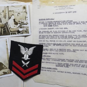May include: A collection of vintage military memorabilia, including black and white photographs of naval personnel and a document with handwritten text. A navy patch with an eagle and crossed swords is also present.