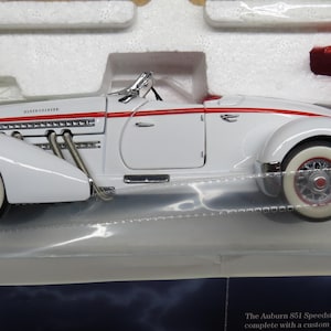 May include: A white Auburn 851 Speedster model car with red accents and a red convertible top. The model has white-walled tires and chrome details. The car is displayed in a protective case.