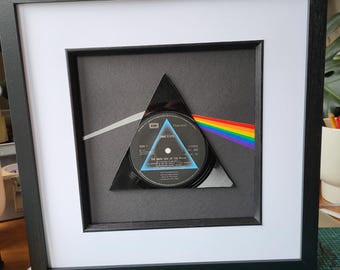 May include: A framed record album with a black triangle design and a rainbow stripe. The album is titled "The Dark Side of the Moon" by Pink Floyd.