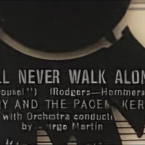May include: A black and white record label with the text "You'll Never Walk Alone" from "Carousel" by Rodgers and Hammerstein. The label also features the text "Gerry and the Pacemakers" with orchestra conducted by  "Irgo Martin".