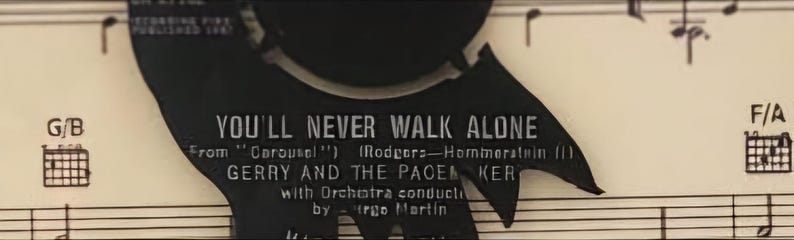 May include: A black and white record label with the text "You'll Never Walk Alone" from "Carousel" by Rodgers and Hammerstein. The label also features the text "Gerry and the Pacemakers" with orchestra conducted by  "Irgo Martin".
