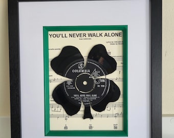 May include: A framed piece of sheet music with a black vinyl record cut into the shape of a shamrock. The record is from the song "You'll Never Walk Alone" by Gerry and the Pacemakers. The music sheet is green and the frame is black.