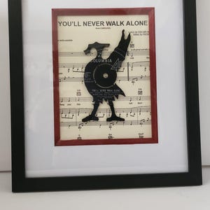 May include: A framed piece of sheet music with a black vinyl record cut out in the shape of a rooster. The music is for the song "You'll Never Walk Alone" from the musical Carousel. The record label is Columbia.