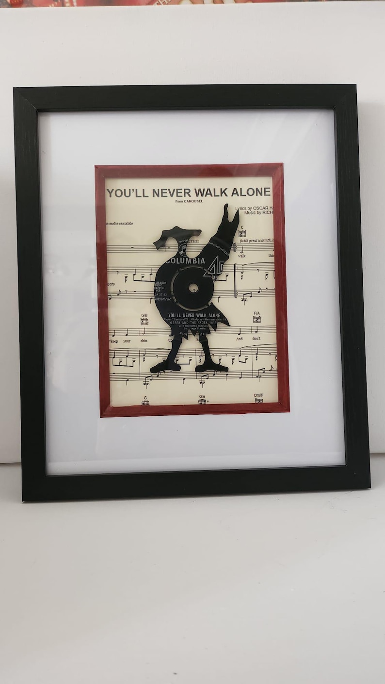 May include: A framed piece of sheet music with a black vinyl record cut out in the shape of a rooster. The music is for the song "You'll Never Walk Alone" from the musical Carousel. The record label is Columbia.