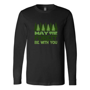 May include: Black long-sleeve shirt with a green and white graphic. The graphic features a row of stylized pine trees above the text "MAY THE FOREST BE WITH YOU". The shirt is made of a soft material.