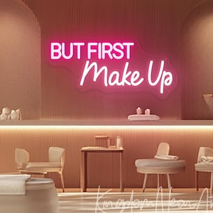 Puede incluir: Un letrero de neón rosa que dice "BUT FIRST Make Up" montado en una pared texturizada. La imagen muestra un interior de salón de belleza, con sillas, mesas y otros elementos decorativos.