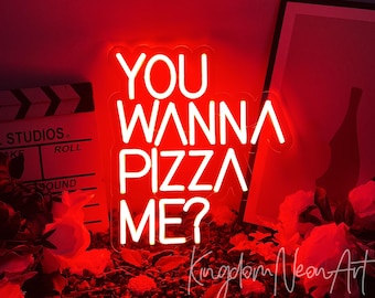 May include: Red neon sign with white lettering that reads "You Wanna Pizza Me?" The sign is sitting on a red surface with flowers and a clapperboard.