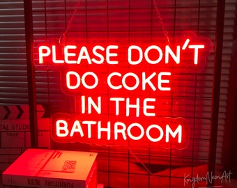 May include: A red neon sign with the text "PLEASE DON'T DO COKE IN THE BATHROOM". The sign is hanging against a dark background. Books are stacked below the sign.