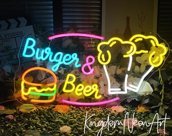 May include: A neon sign with the words "Burger & Beer" in bright blue and pink. A neon burger and beer mug are also featured. The sign is surrounded by flowers and greenery, with the text "Kingdom Neon Art" at the bottom.