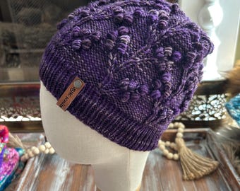 May include: Purple knitted beanie with a textured pattern and a brown leather label that says "SKIRKIS".