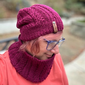May include: A burgundy knitted hat and matching cowl neck scarf. The hat has a leather tag with the text "SJK Knits".