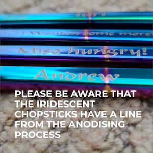 May include: A set of five iridescent stainless steel chopsticks with personalised engravings. The chopsticks are arranged in a stack, with the engravings facing the viewer. The engravings read "I'll eat some more", "Also hungry!" and "Andrew". The text "PLEASE BE AWARE THAT THE IRIDESCENT CHOPSTICKS HAVE A LINE FROM THE ANODISING PROCESS" is visible below the chopsticks.