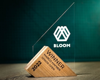 May include: A wooden and glass award with the text "WINNER" and "MARCO HAFNER SENIOR OPEN 2022" on the wooden base. The glass portion features a white geometric logo with the word "BLOOM" below it.