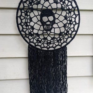 May include: Black crochet dreamcatcher with a skull design and black fringe hanging from the bottom.