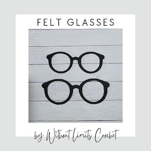 May include: Two pairs of black felt glasses are displayed on a white wooden background. The text "FELT GLASSES" is at the top, and the text "by Without Limits Crochet" is at the bottom. The glasses are round with thick black frames.