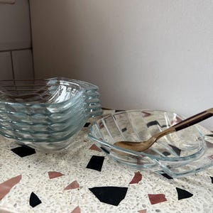 May include: A collection of clear glass leaf-shaped dishes. One dish contains a small spoon with a brown handle. The dishes are on a terrazzo surface with black, pink, and white chips.