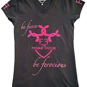 May include: Black v-neck t-shirt with pink glitter lettering that reads "be fierce" and "be ferocious" with a stylized logo in the centre that reads "FF The Femme Fatale".