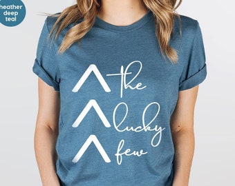 May include: A blue t-shirt with white text that reads "The Lucky Few" with three white chevron shapes above the text.