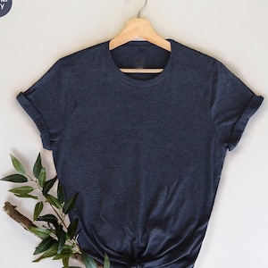 May include: A navy blue heather t-shirt with rolled sleeves hangs on a wooden hanger. The shirt is knotted at the bottom. The words "the PRINT SHOP here" are at the bottom left.
