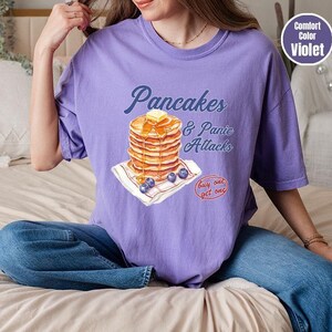 a woman sitting on a bed with a stack of pancakes on her shirt