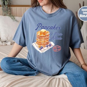a woman sitting on a bed with a stack of pancakes on her shirt
