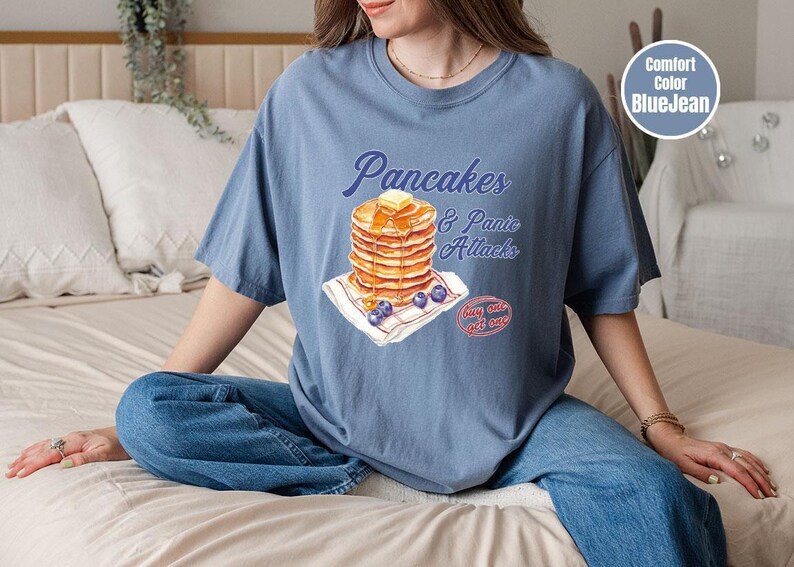 a woman sitting on a bed with a stack of pancakes on her shirt